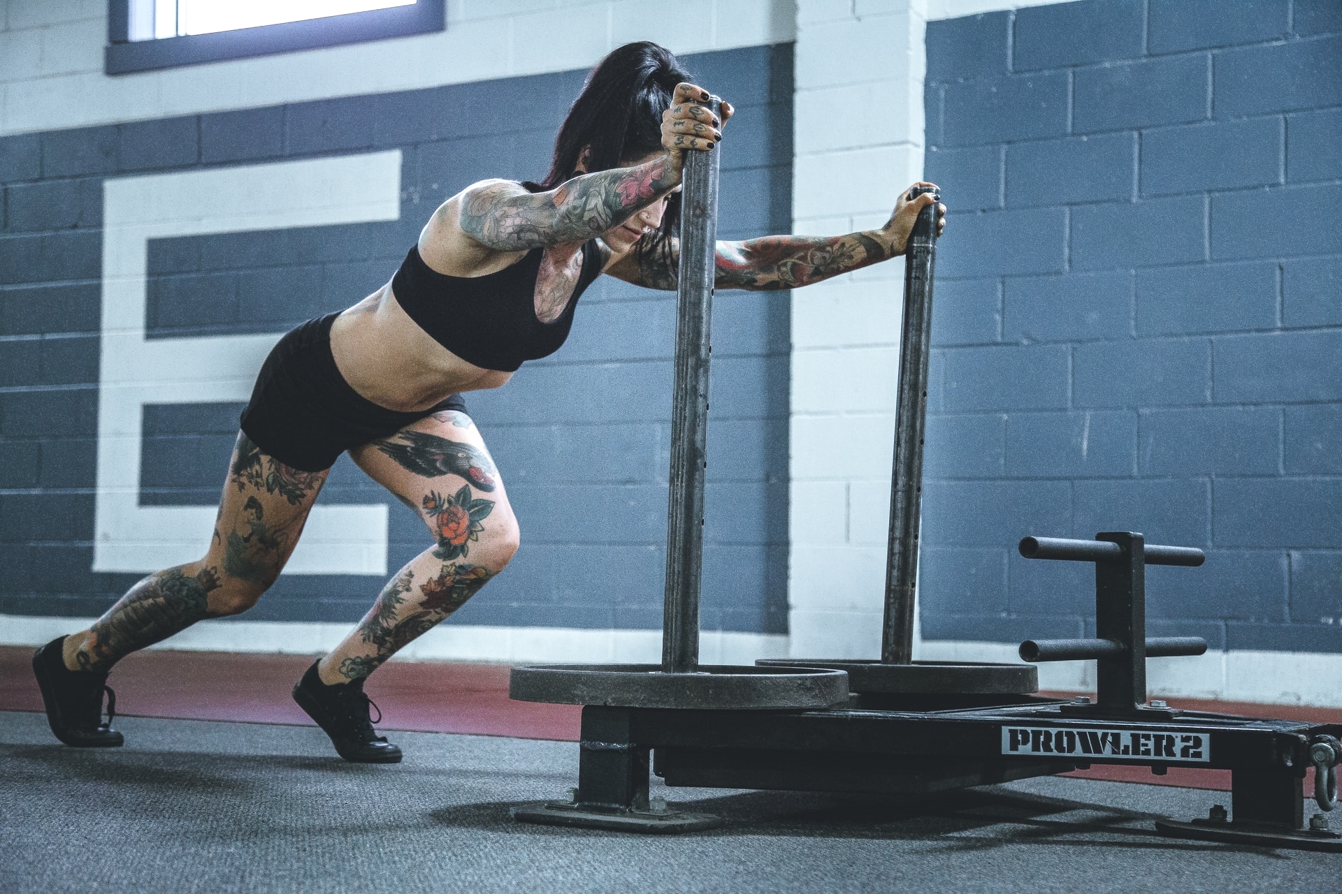 Tattoed woman doing a CrossFit exerise workout using the sled