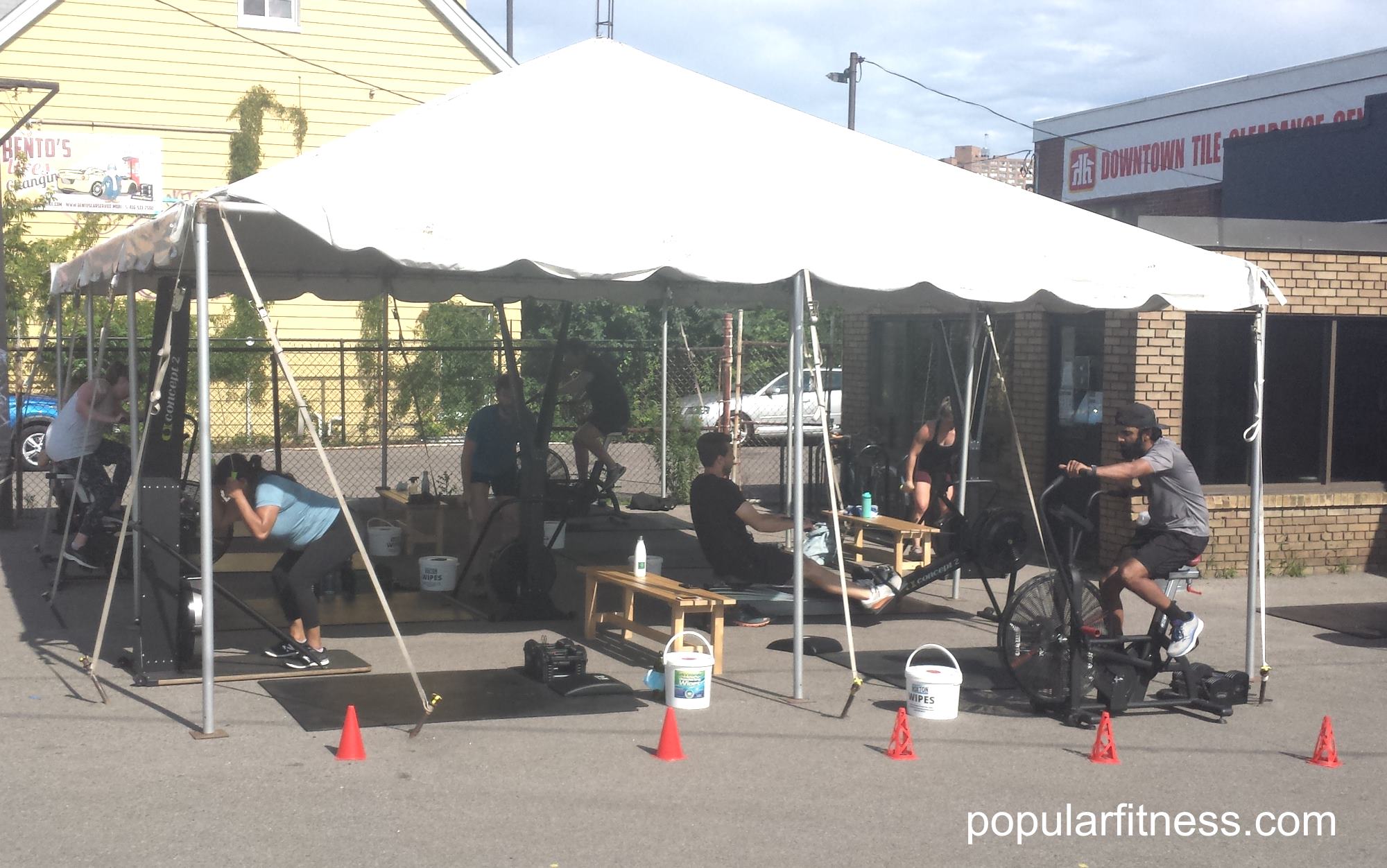 People exercising outdoors under a tent at an outdoor gym setup.