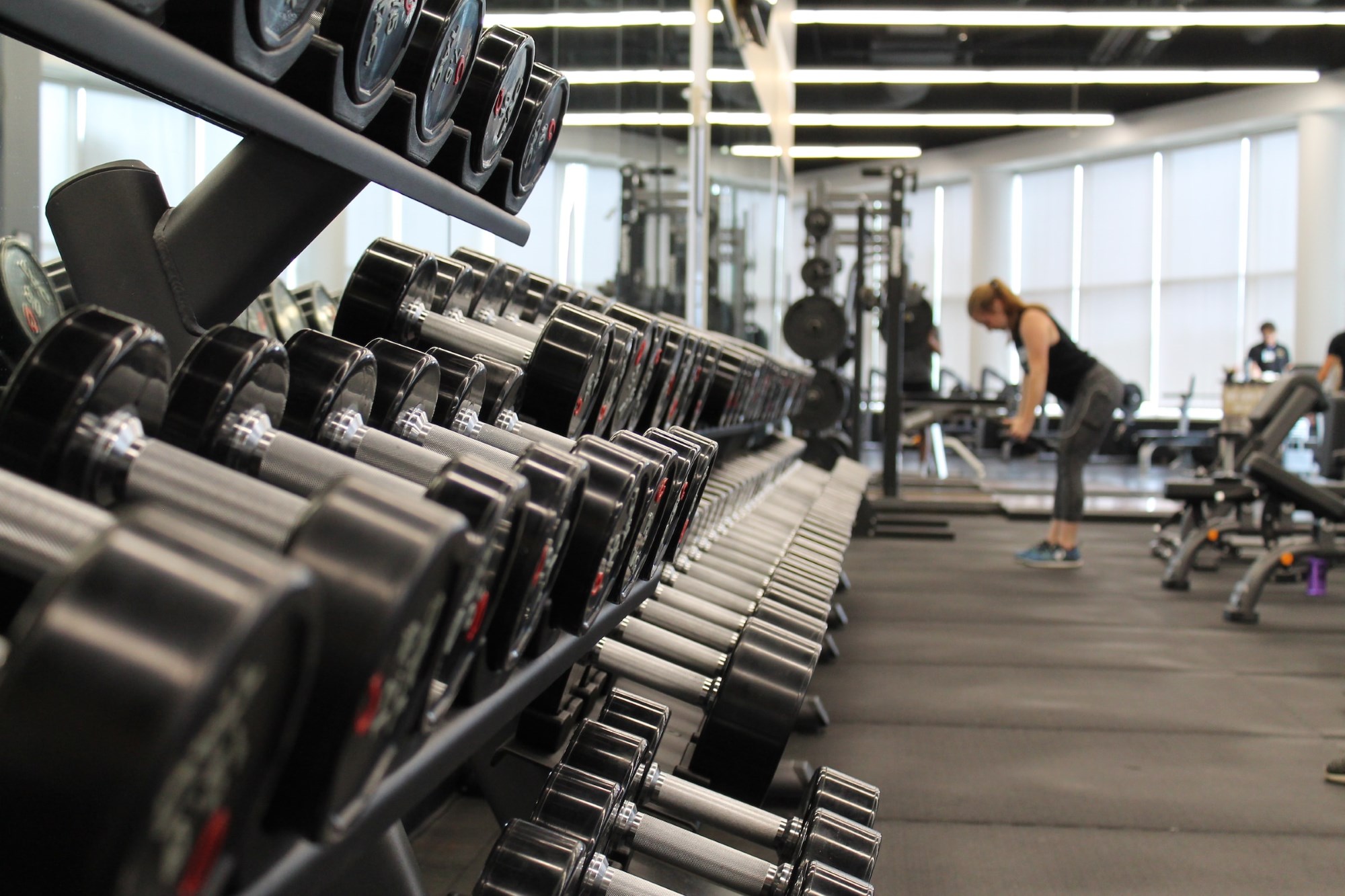 An open floor plan for a gym - dumbbell rack and woman weight training