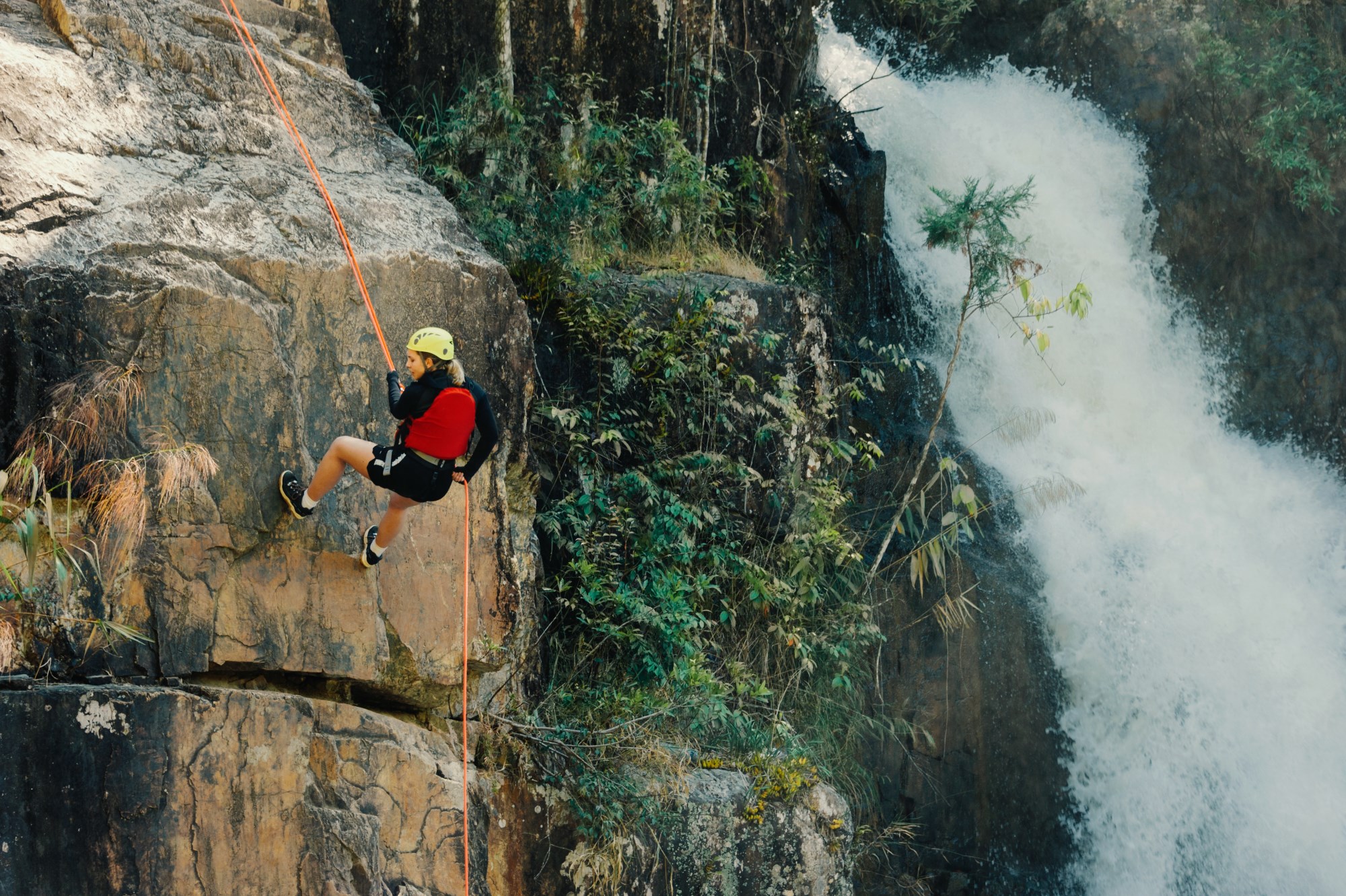 A woman rock climber enjoying the outdoor sport of rock climing near a waterfall.