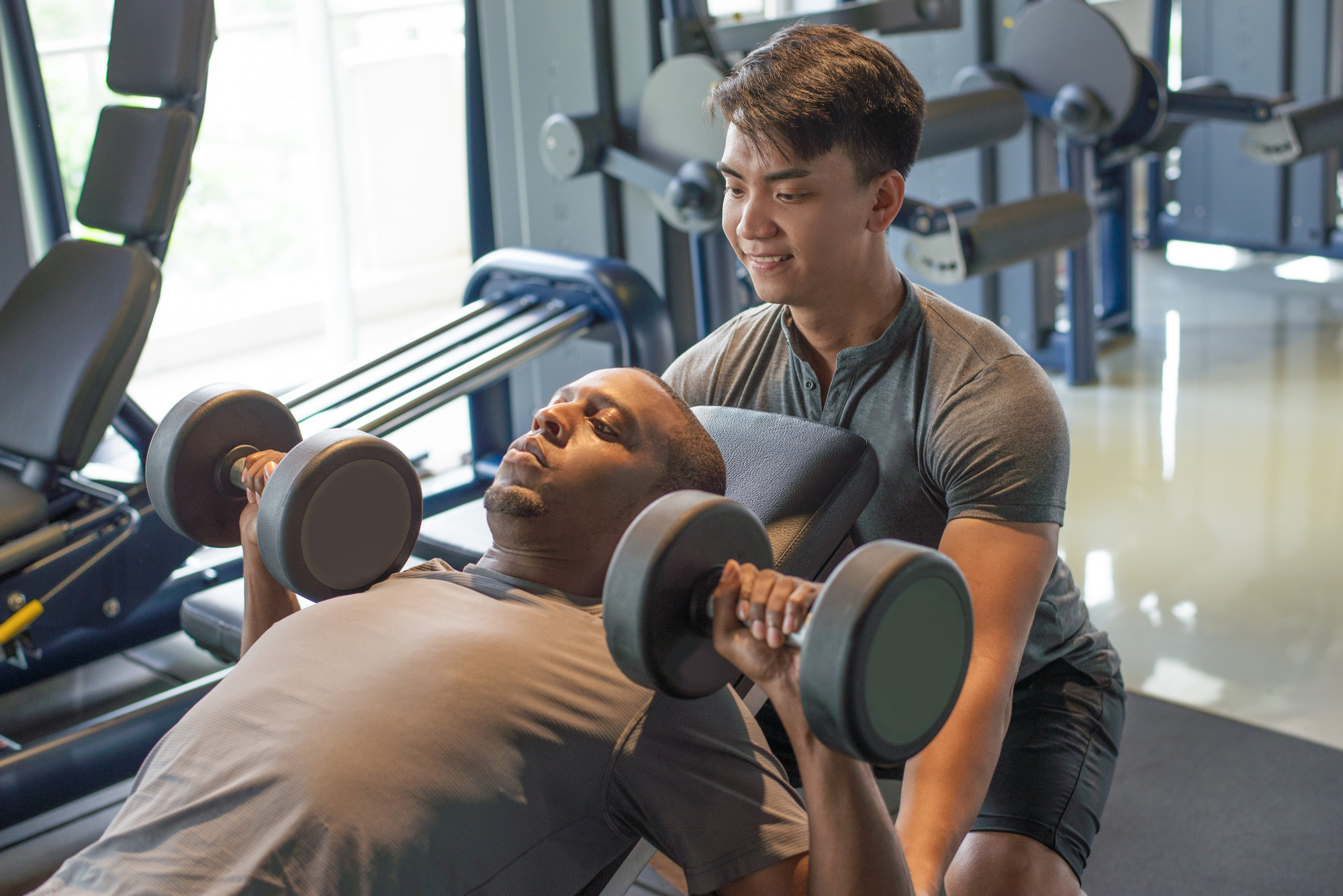 Personal trainer training client while he does the incline chest press