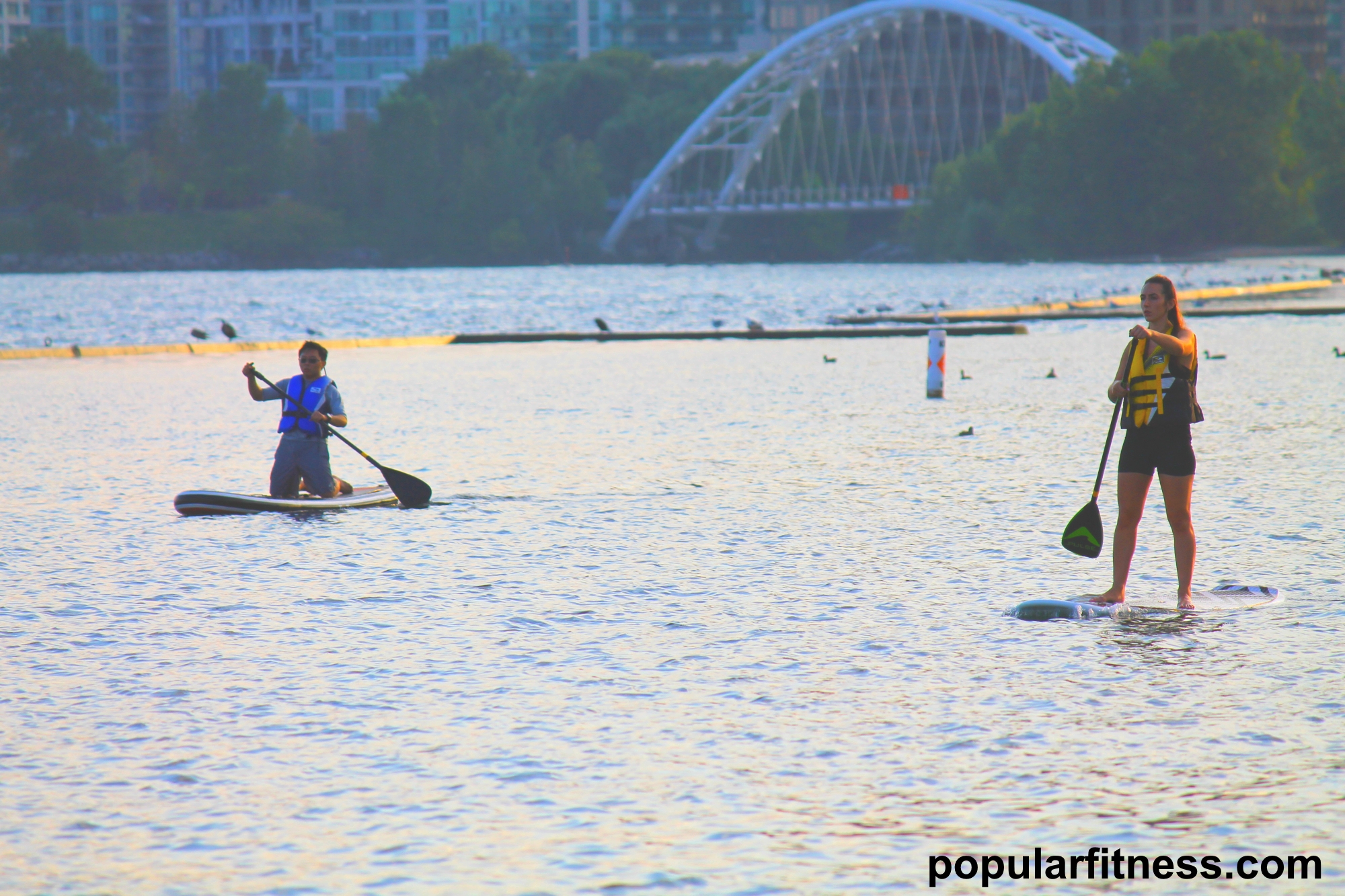 Paddle boarding on a paddleboard on the lake while standing up - photo by popular fitness