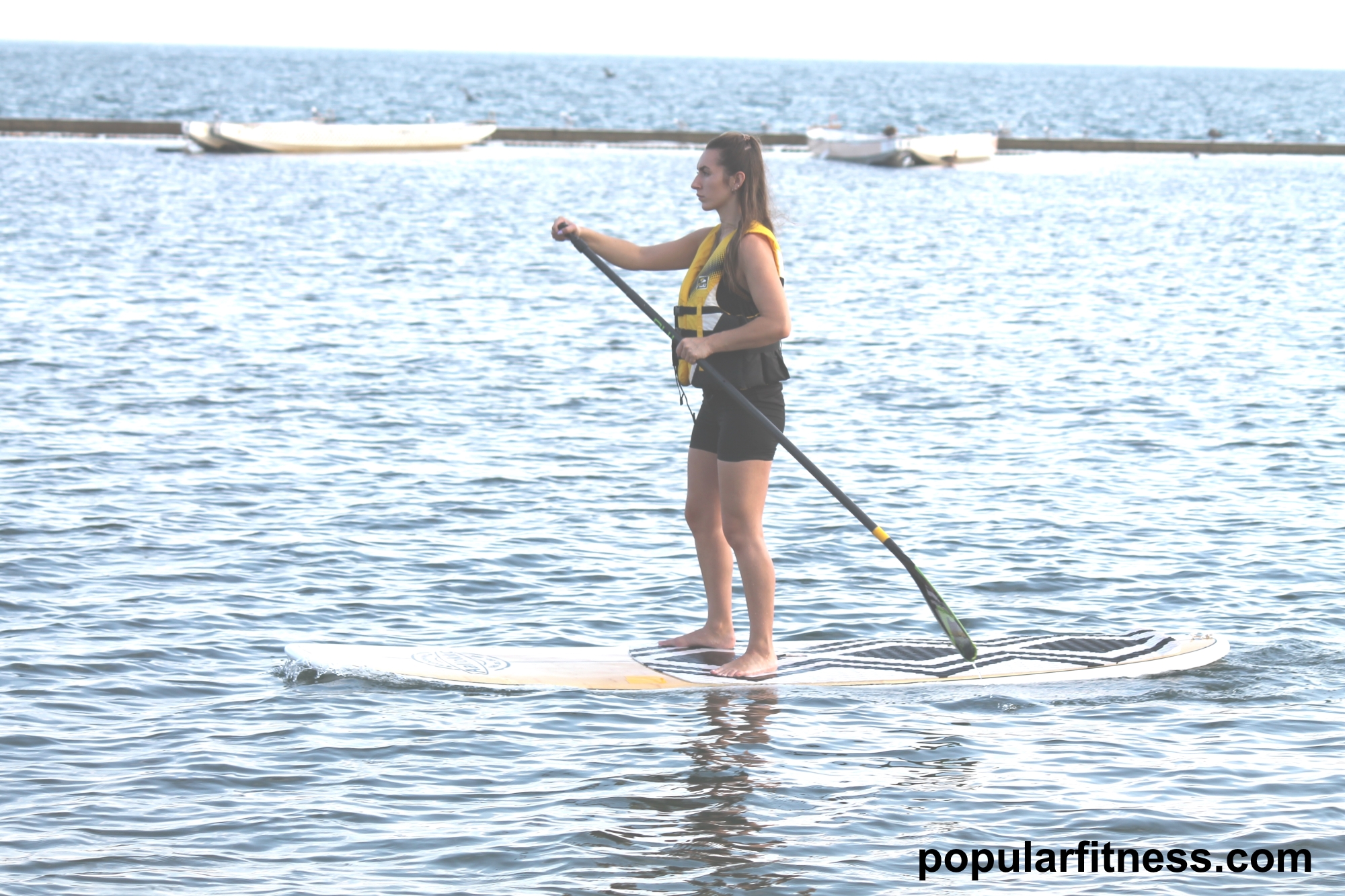 Paddle boarding on a paddleboard on the lake while standing up - photo by popular fitness