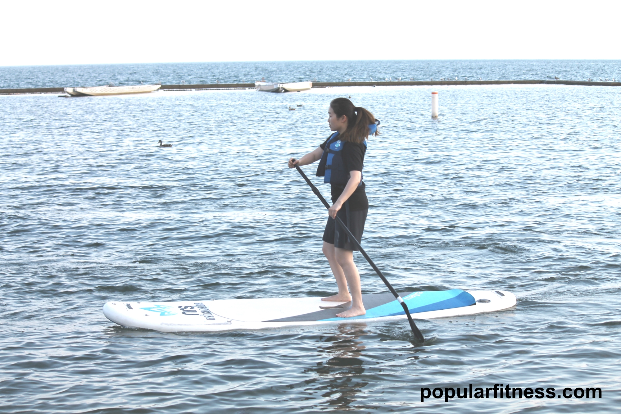 Paddle boarding on a paddleboard on the lake while standing up - photo by popular fitness