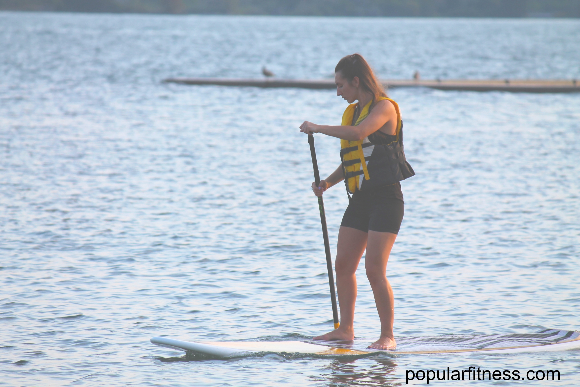 Paddle boarding on a paddleboard on the lake while standing up - photo by popular fitness