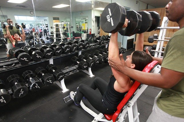 Woman with the help of a spotter strength training using weights - dumbbells