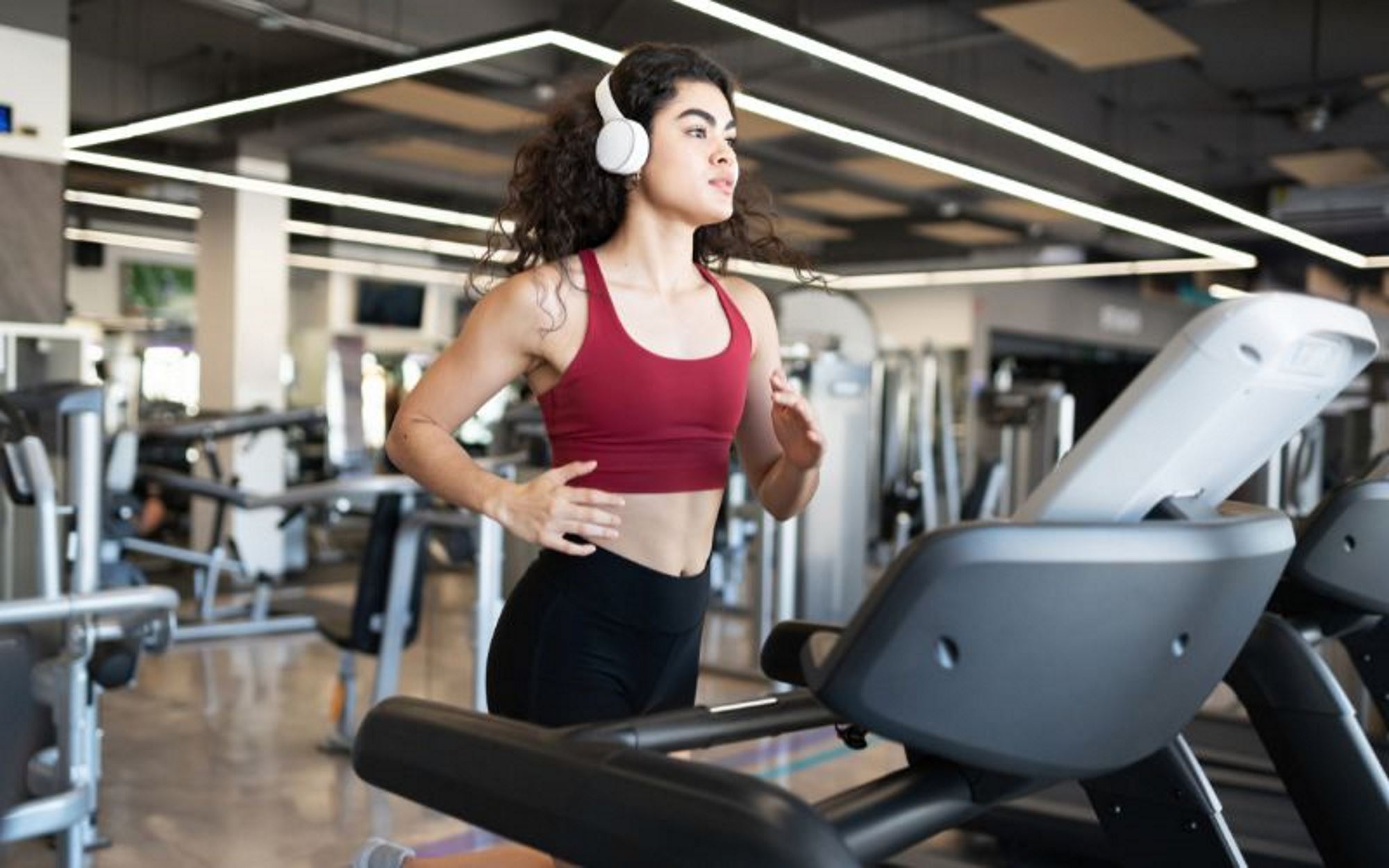 A woman exercising while listening to music on her headphones. Running on a treadmill at the gym.